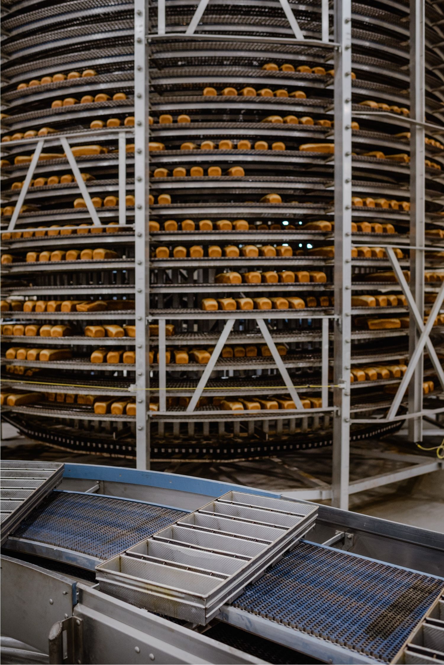 A multi-tier cooling spiral loaded with bread, with American Pan bread pans on the conveyor in the foreground
